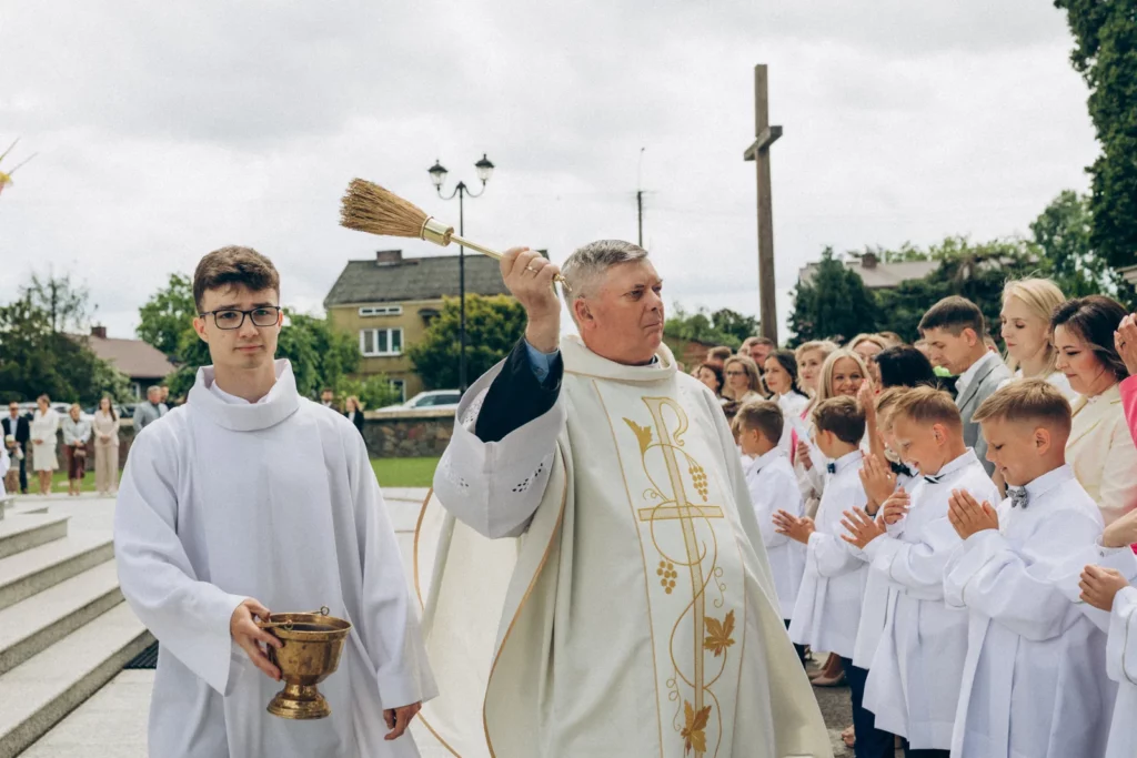 Ksiądz błogosławi dzieci zgromadzone przed kościołem