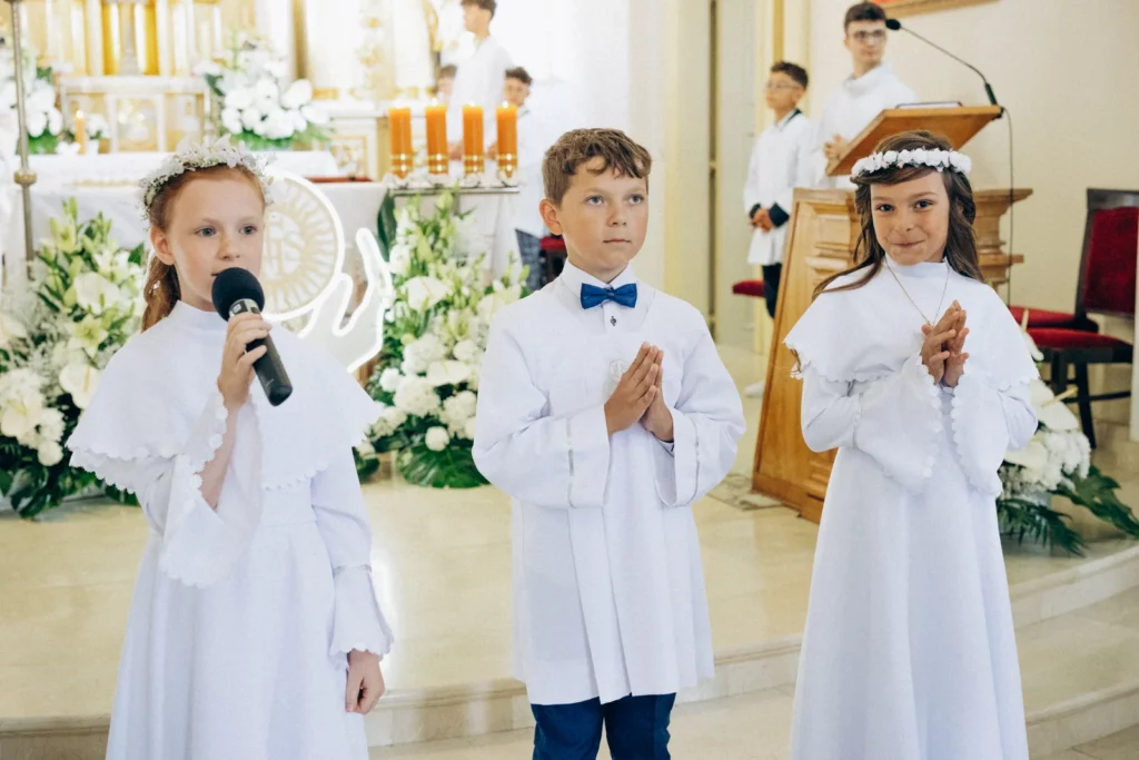 Dzieci czytają przy mikrofonie podczas uroczystości komunijnej