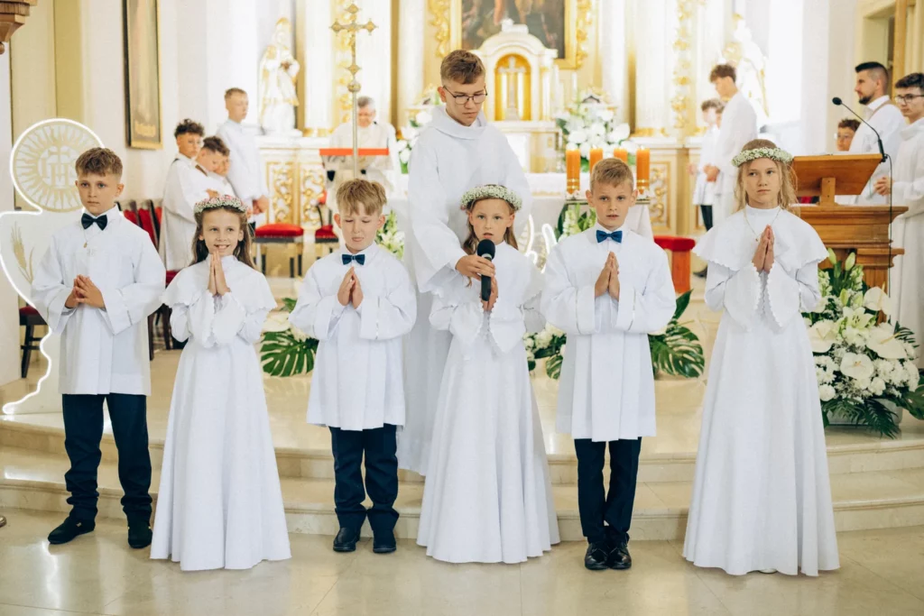 Dzieci w strojach komunijnych stoją przy ołtarzu