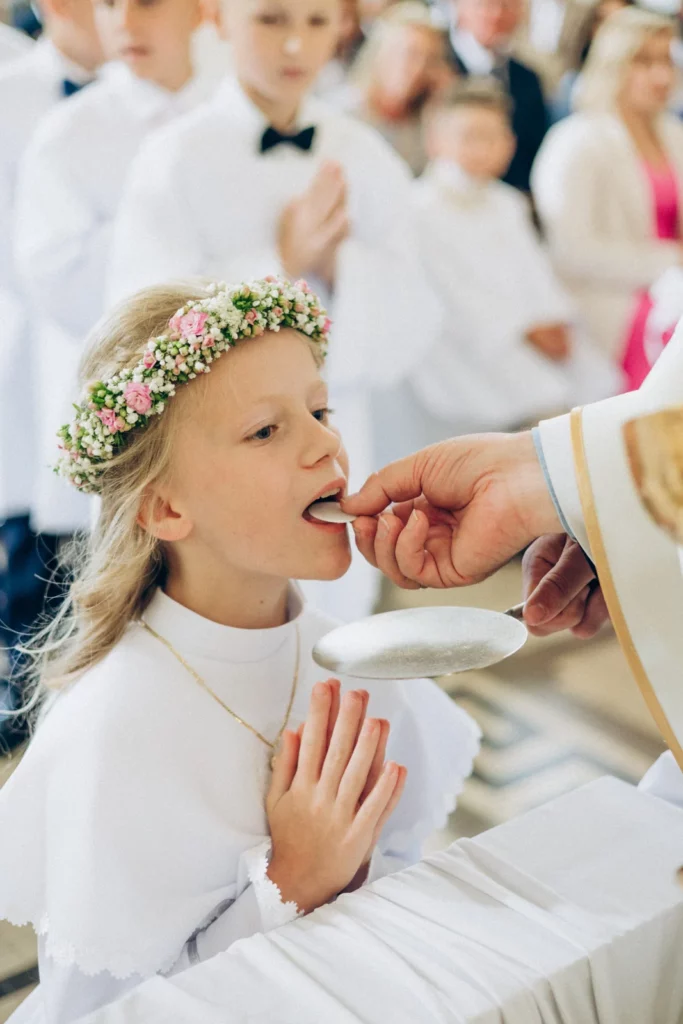 Dziewczynka w wianku przyjmuje Pierwszą Komunię Świętą