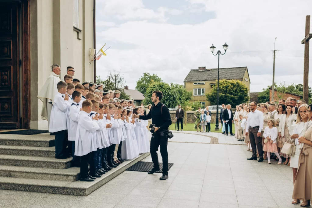 Fotograf ustawia dzieci do wspólnego zdjęcia przed kościołem
