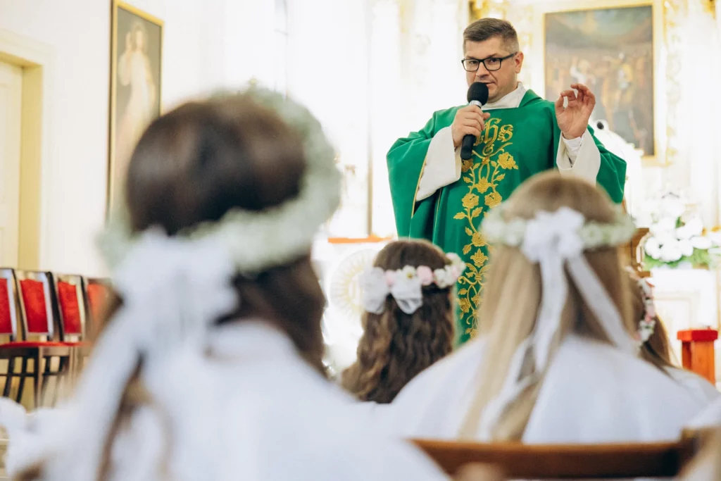 Ksiądz przemawia do dzieci podczas uroczystości komunijnej