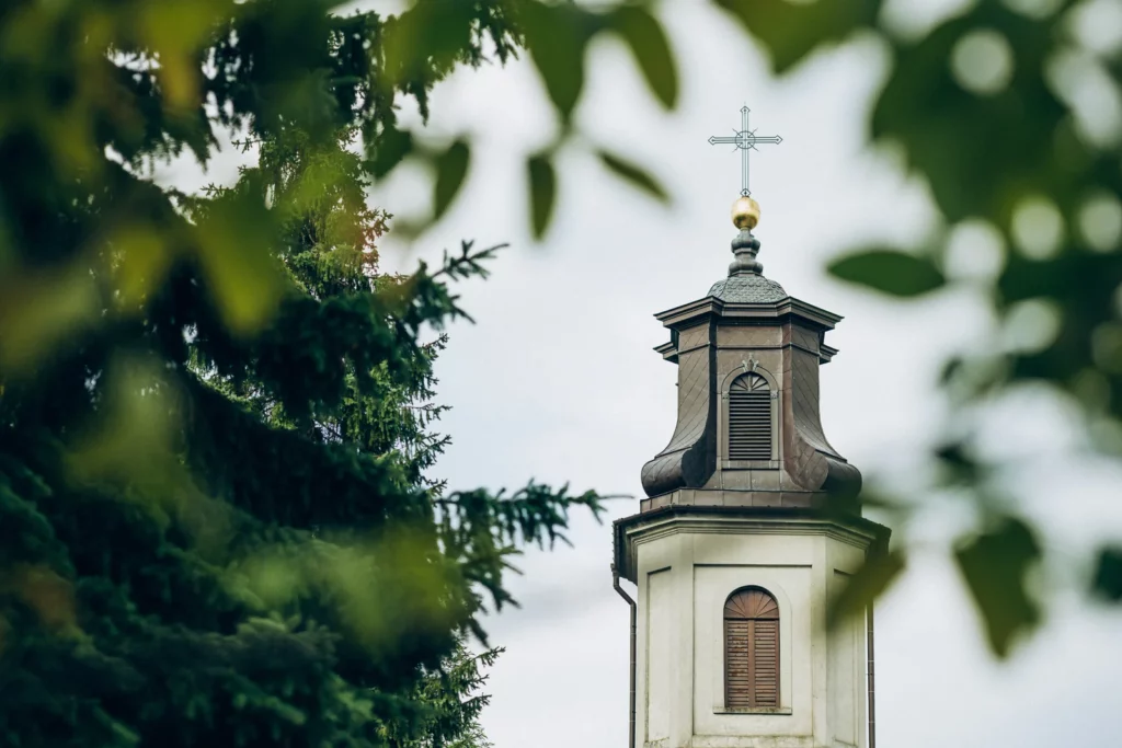 Wieża kościoła widziana między zielonymi gałęziami