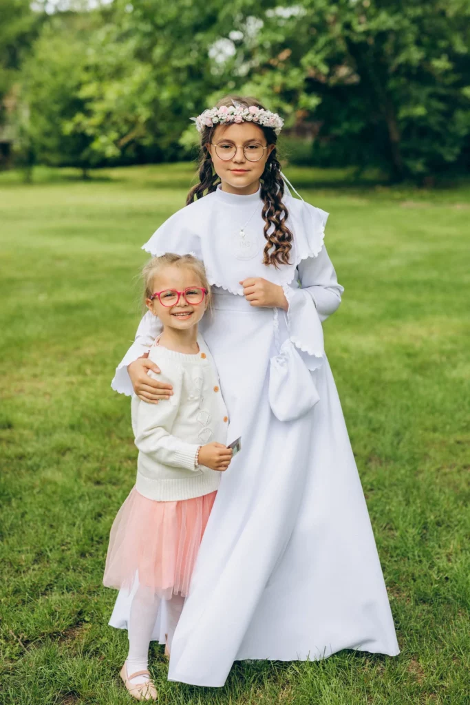 Dziewczynka w stroju komunijnym obejmuje młodszą dziewczynkę