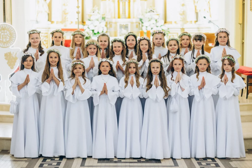 Dziewczynki w białych strojach komunijnych pozują przed ołtarzem