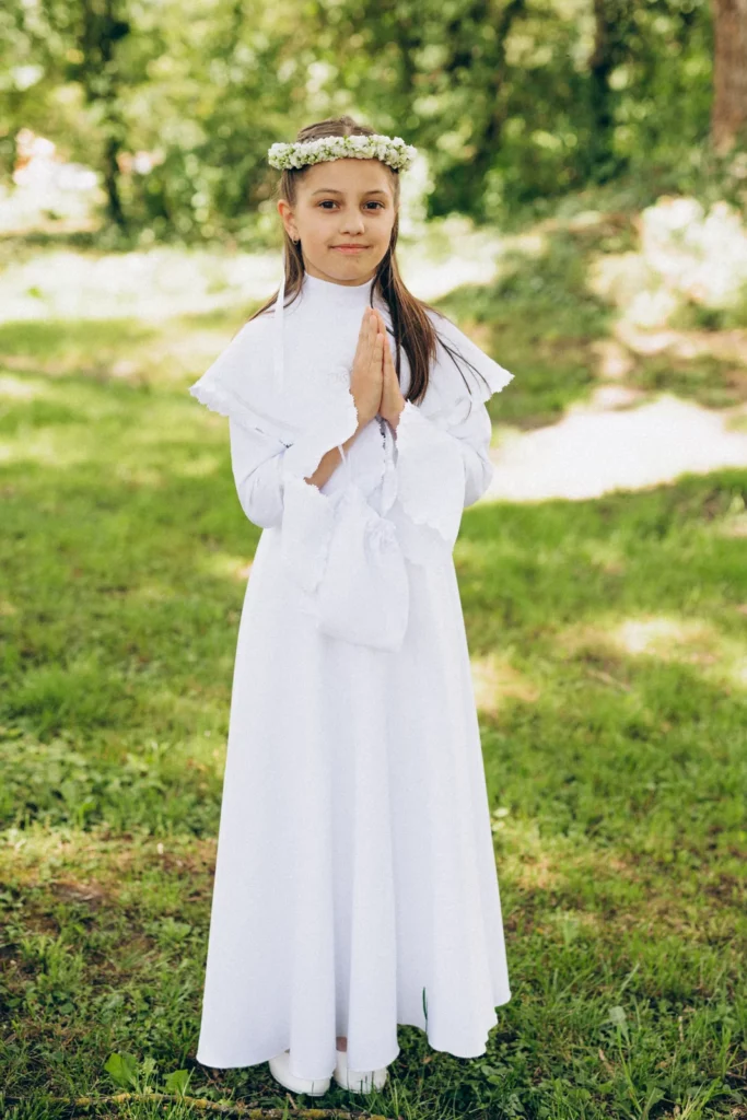 Dziewczynka w białej albie pozuje na tle zieleni