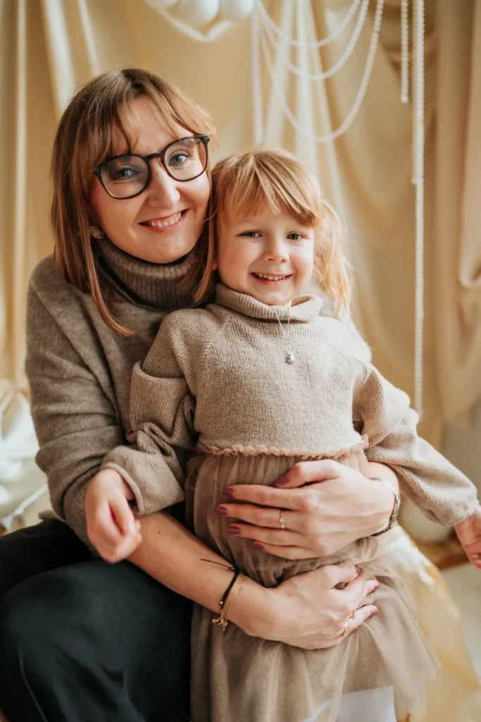Mama przytula córkę na tle jasnej świątecznej dekoracji