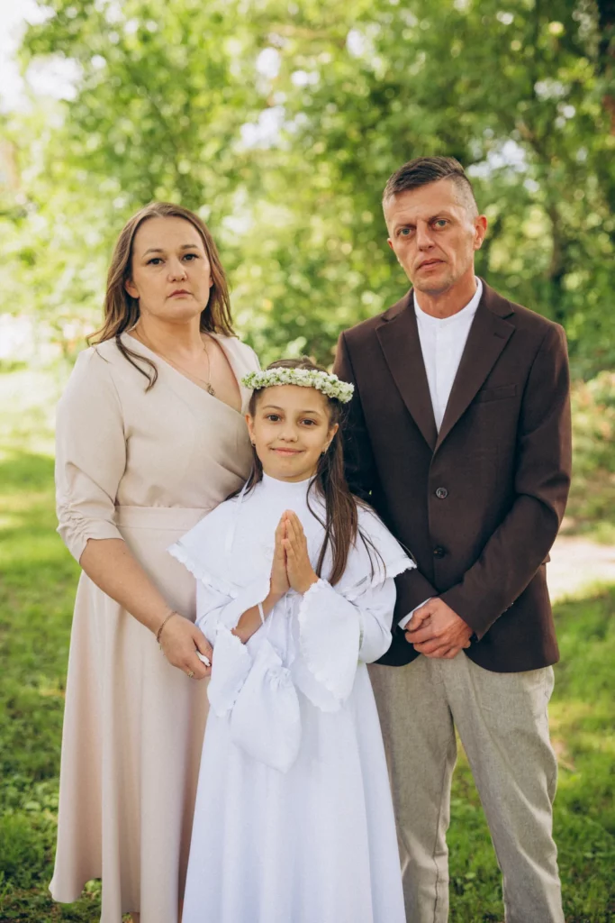 Dziewczynka w stroju komunijnym z kobietą i mężczyzną w plenerze